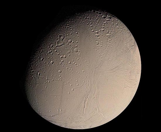Esta é Encélado, uma das luas de Saturno. Imagens da sonda Cassini indicam que existam reservatórios de água líquida abaixo da crosta gelada do satélite. A água seria expelida à superfície por meio de gêiseres de vapor e gás.