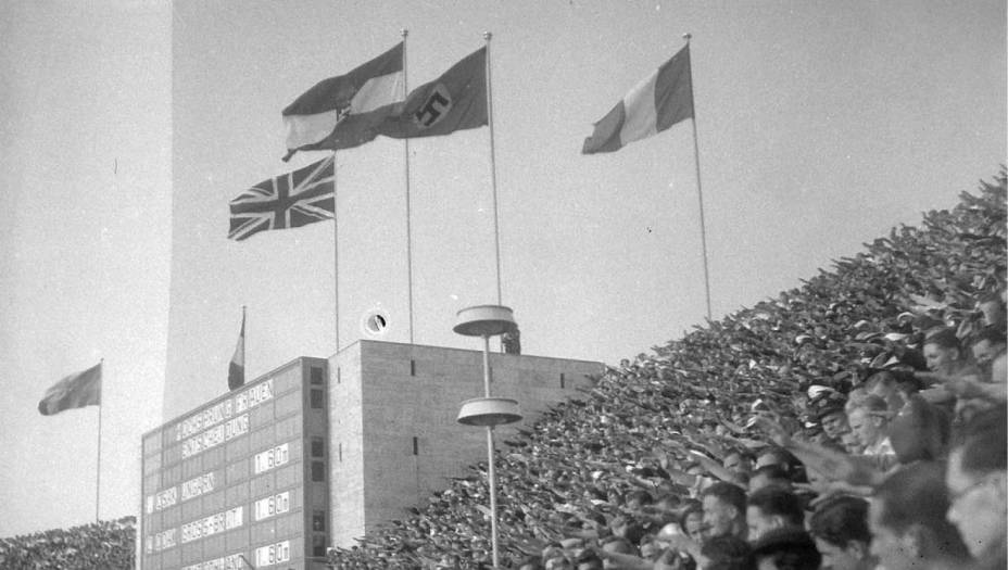 Quando o Comitê Olímpico percebeu que havia errado feio, decidiu continuar com os planos de sediar a olimpíada em Berlim - mesmo sob protestos de vários países. A ideia era desmascarar o regime nazista, escancarando a discriminação para o mundo, mas Hitler foi mais esperto: em cima da hora, permitiu que todas as etinias participassem dos jogos, e mandou esconder marcas antissemitas, como placas que proibiam a entrada de judeus em estabelecimentos comerciais - só em Berlim. Essa restrição não impediu que manifestações nazistas, como o "heil Hitler", acontecessem em pleno estádio olímpico.