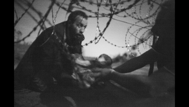 Um homem passa um bebê por uma cerca na fronteira entre a Hungria e a Sérvia. A imagem, do australiano Warren Richardson, retrata um momento de esperança em meio à trágica crise dos refugiados sírios que tentam escapar do Estado Islâmico. A foto foi considerada "a imagem do ano" pelo World Press Photo.