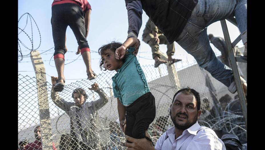 A onda de refugiados sírios e de outros países do Oriente Médio rumo a Europa foi o tema mais lembrado pelo World Press Photo. Nesta foto, um pai tenta ajudar sua filha a passar pela cerca que os separa do território turco. A imagem deu o terceiro lugar na categoria Notícias para o fotógrafo turco Bülent Kiliç.