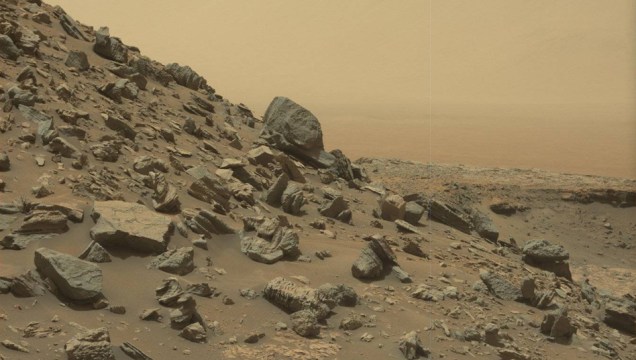 Aqui, o Curiosity já está bem alto no Monte Sharp. Ele conseguiu capturar, lá longe, a superfície de uma cratera chamada Gale (talvez fique meio difícil de enxergar por causa da poeira, mas ela está à direita na foto)