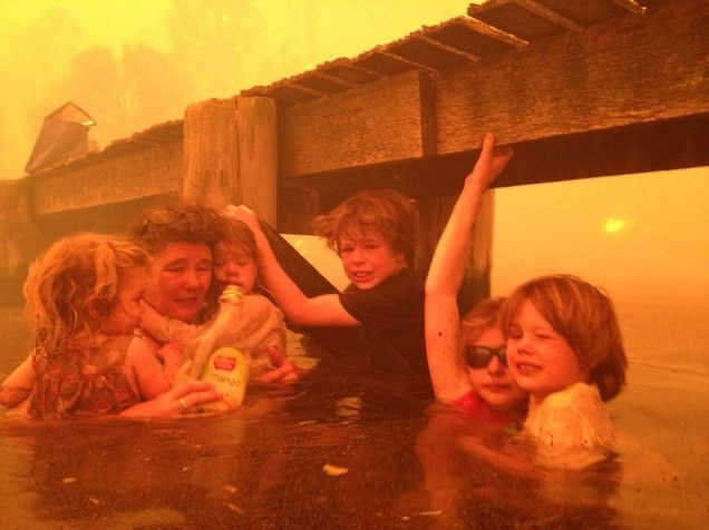 Tammy Holmes e seus netos se protegem em um cais fugindo de um incêndio florestal que se alastrou até a cidade australiana de Dunalley. O fotógrafo é o avô das crianças, Tim Holmes, que decidiu levá-los para água.