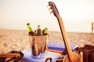 Beer bottles in a bucket of ice in the sand on a tropical beach. Guitar,backpack and everything is ready for party.
