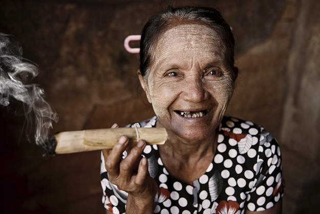 Happy old wrinkled Asian woman smoking