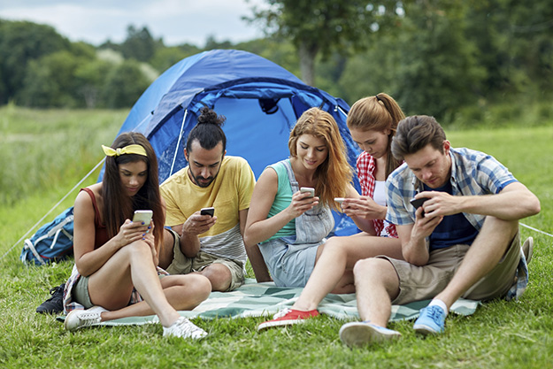 friends with smartphone and tent at camping