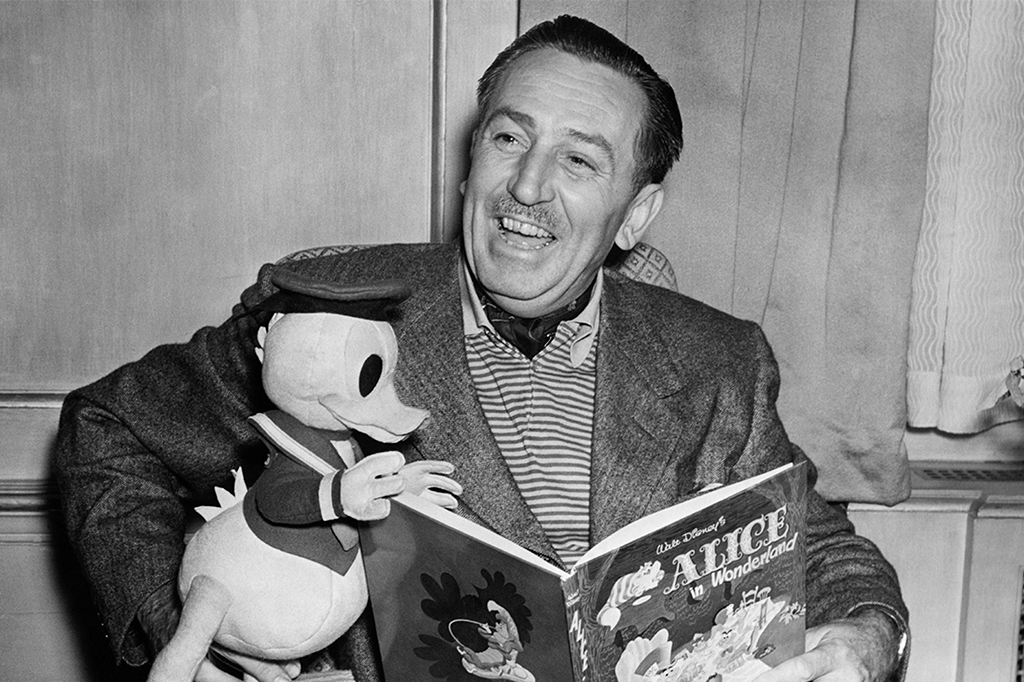 Foto em preto e branco de Walt Disney segurando uma pelúcia do Pato Donald e um exemplar do livro Alice no País das Maravilhas