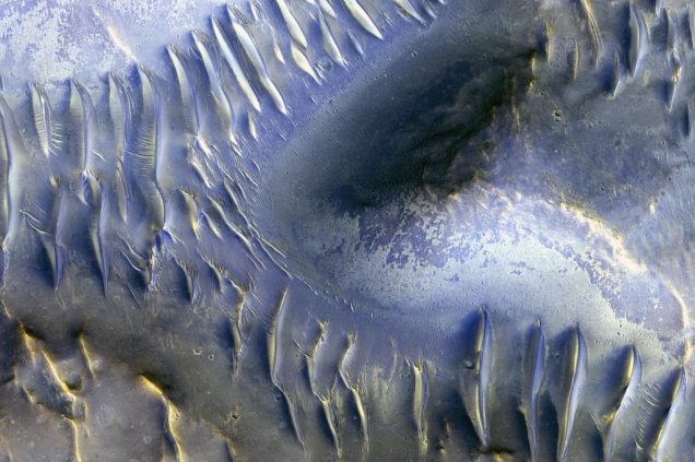 Isto é Marte. Essas ondinhas que aparecem abaixo, na verdade, são dunas de areia que são formadas por um vento que vai do norte (no canto esquerdo da foto) ao sul. A grande sacada da imagem é mostrar que uma montanha marciana, localizada no meio da foto, conseguiu bloquear essas correntes de vento, impedindo a criação das dunas na sua parte de trás.