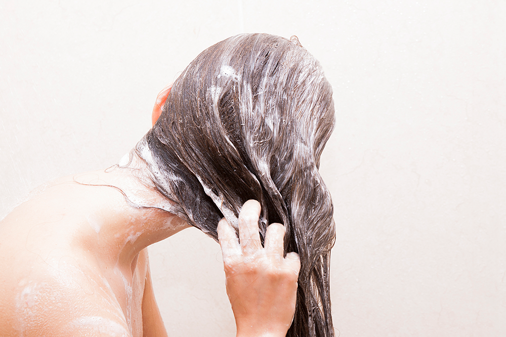Mulher meio de costas lavando o cabelo.