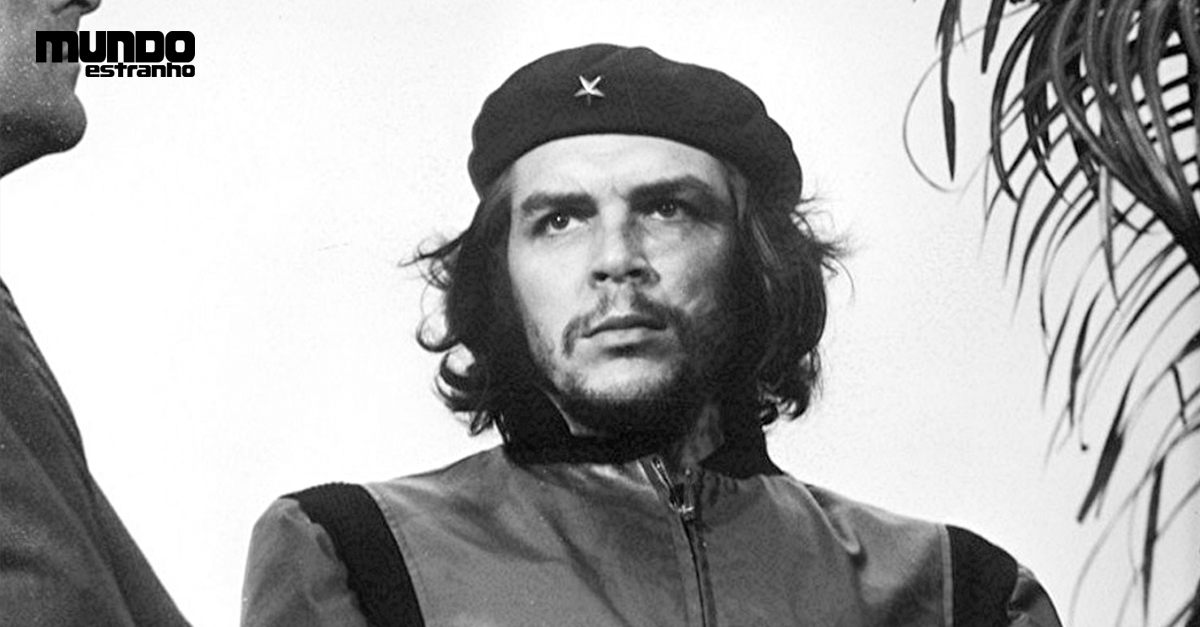Retrato em preto e branco de Che Guevara, com boina preta e estrela, barba e cabelo comprido. Ele veste uma jaqueta escura com zíper e olha para cima, com expressão séria. No canto superior esquerdo, o logo MUNDO estranho. À direita, folhas de palmeira.