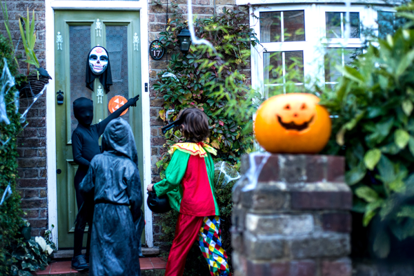 Foto de crianças fantasiadas na frente de uma casa decorada para o Halloween, há uma abóbora com rosto do lado, elas estão tocando a campainha.