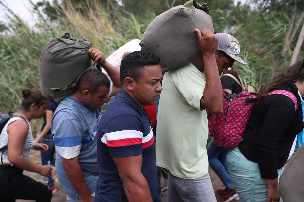 Imigrantes venezuelanos na fronteira com a Colômbia. Eles estão carregando sacolas sobre os ombros.