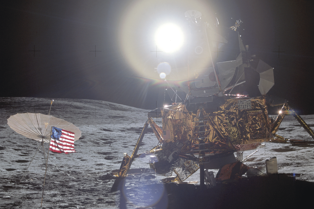O módulo Antares, que pousou numa região com oito graus de inclinação. Ele é dourado, e há uma bandeira dos EUA hasteada à esquerda. Ao fundo, o Sol.