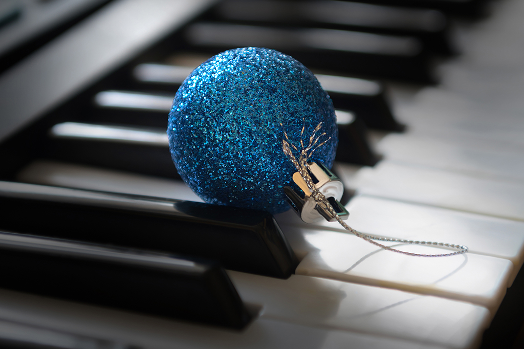 Enfeite de natal em formato de bola azul com glitter em cima de teclas de piano.