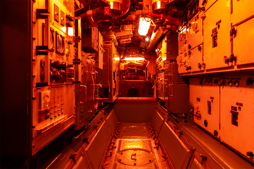 Interior de um submarino, com maquinário iluminado por uma luz vermelha.