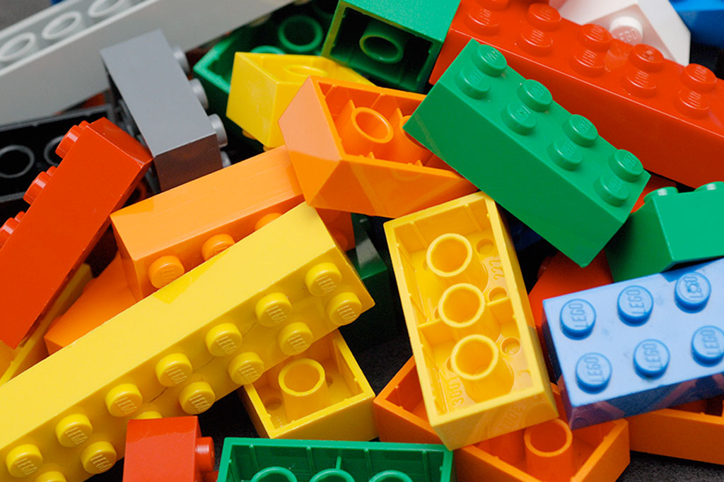 peças coloridas de Lego: amarelas, verdes, laranjas e azuis.