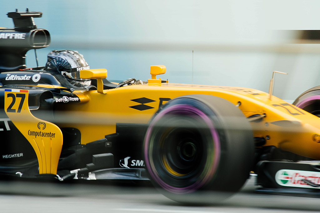 Zoom em um carro de corrida amarelo, com o piloto dentro, em alta velocidade.