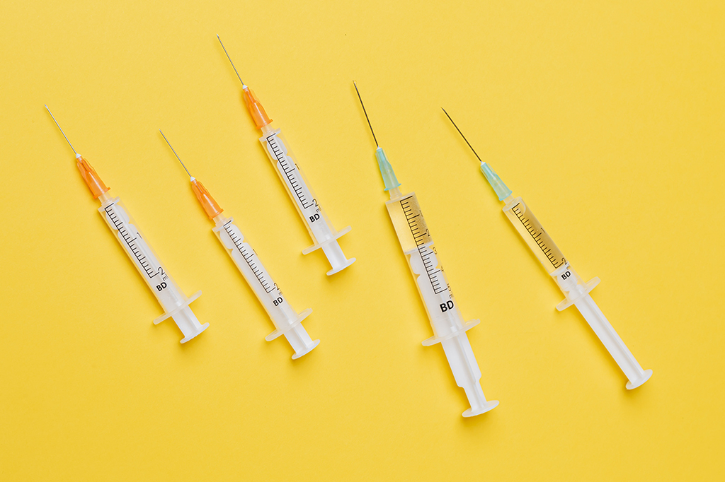 Cinco seringas de vacina em uma superfície amarela.