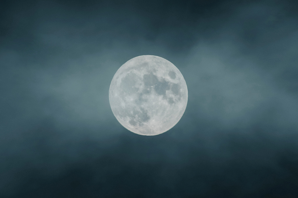 Lua cheia no centro da imagem, com nuvens ao redor.