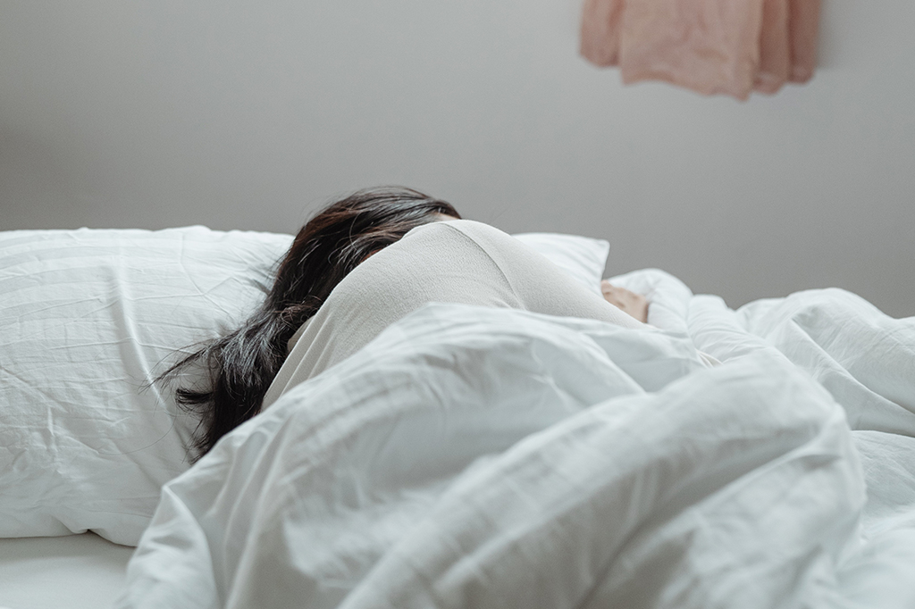 Mulher de cabelos escuros deitada na cama, de costas para a câmera.
