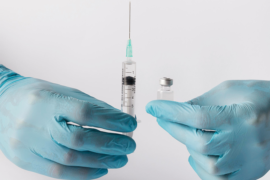 Pessoa de frente segurando uma seringa com a mão direita e uma ampola de vacina com a mão esquerda.