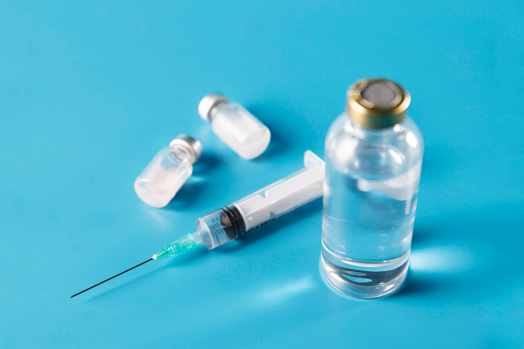 Ampolas e seringa de vacina vistos de cima, em uma superfície azul.