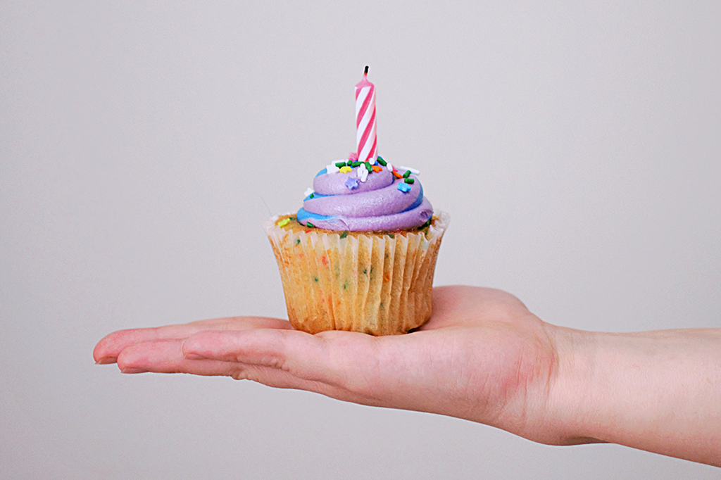 Uma mão segurando um cupcake com uma velinha de aniversário.
