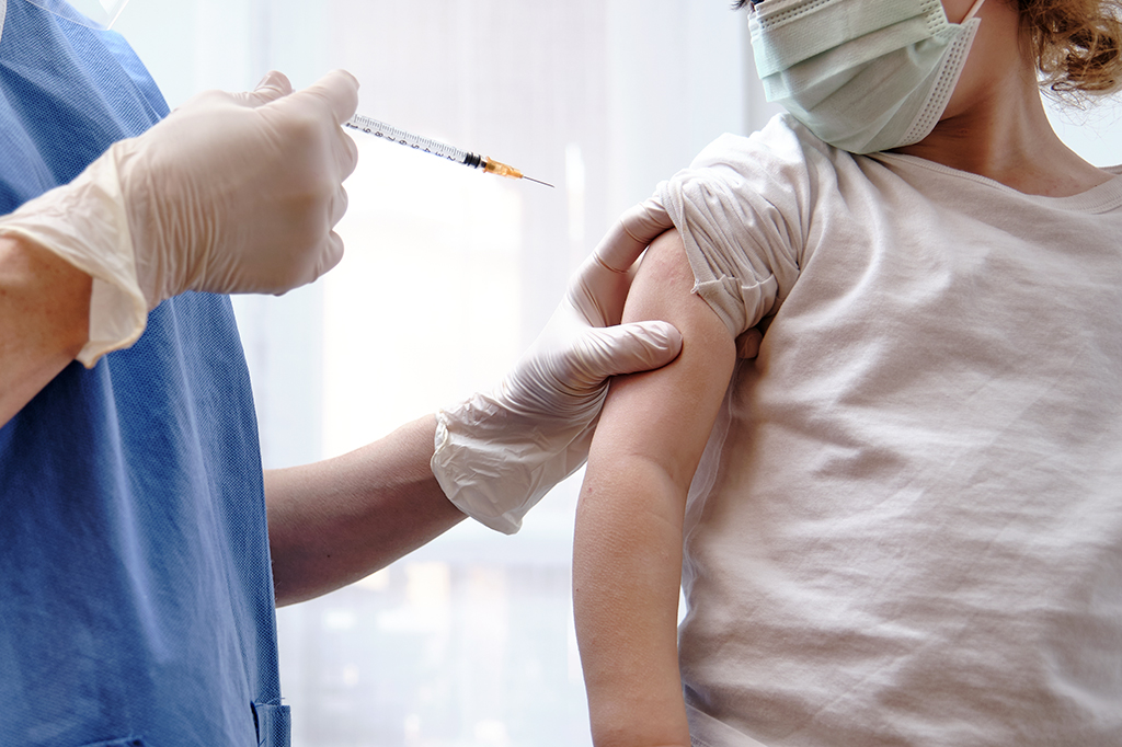Profissional da saúde aplicando vacina no braço direito de uma criança.