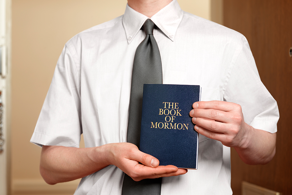 Foto de um homem brancom, vestindo camisa e gravata, segurando o Livro de Mórmon.