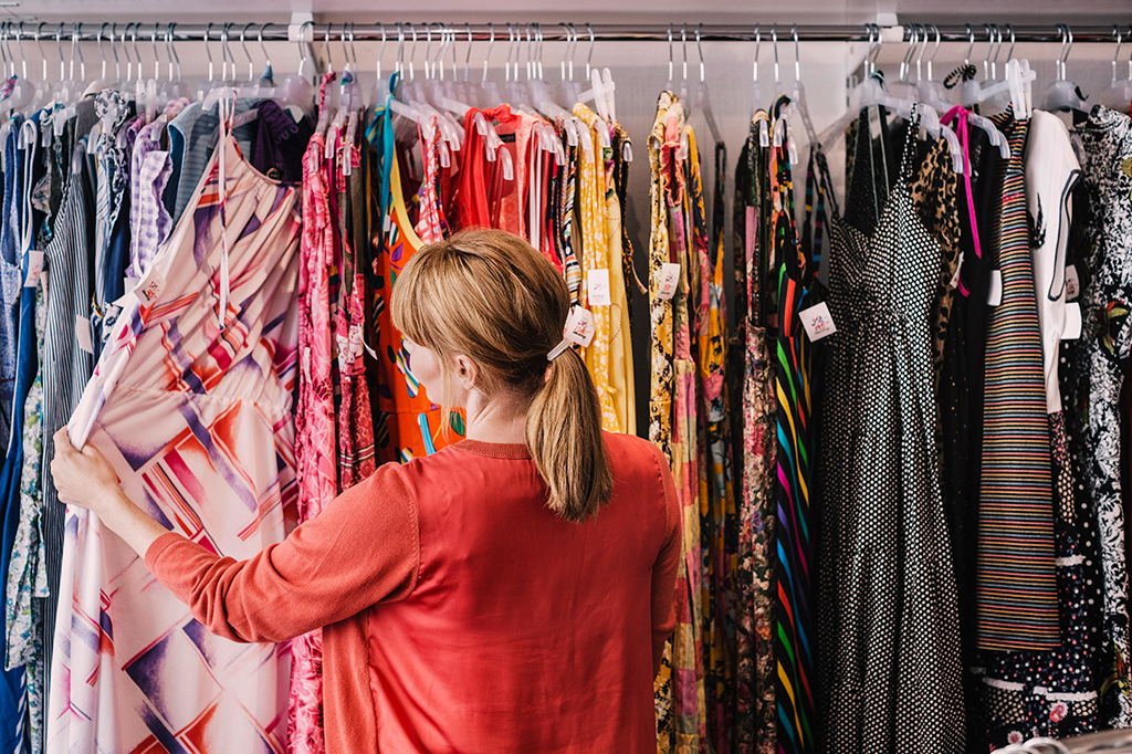 Foto de uma mulher vendo vestidos numa arara, em uma loja de roupas.