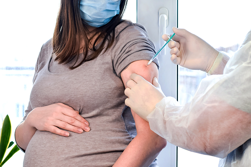 Mulher grávida recebendo vacina no braço esquerdo.