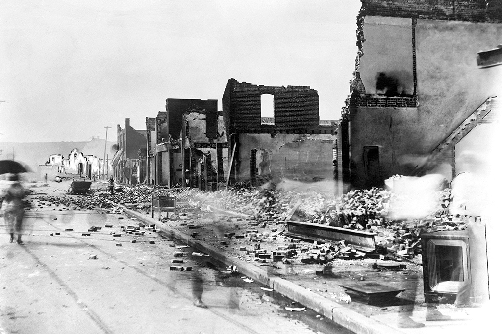 Foto em preto e branco mostra uma rua com casas e comércios destruídos, durante o massacre racial em Tulsa, em 1921.