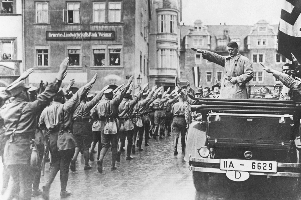 O líder nazista Adolf Hitler no carro, à direita, recebe a saudação enquanto os paramilitares marcham na praça do mercado em Weimar, Alemanha, 13 de novembro de 1930.