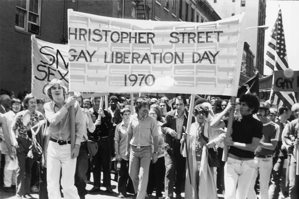 Foto da primeira parada do Orgulho LGBT com pessoas carregando a faixa "Christopher Street Gay Liberation Day 1970".