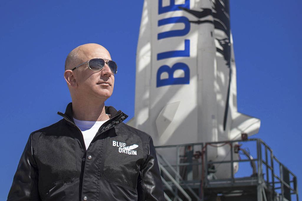 Jeff Bezos em primeiro plano com foguete da Blue Origin ao fundo.