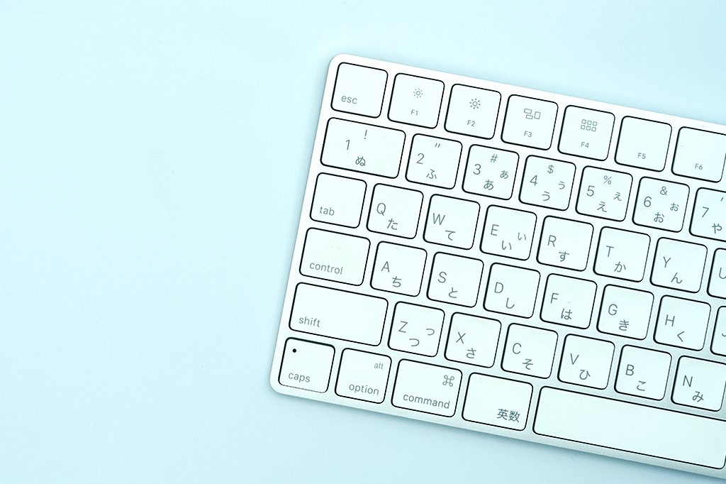 Foto de um teclado de computador japonês branco, em um fundo azul claro.