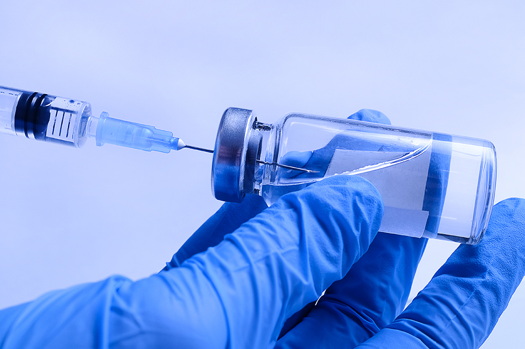 Zoom mostrando uma mão de luva enchendo uma seringa de vacina.
