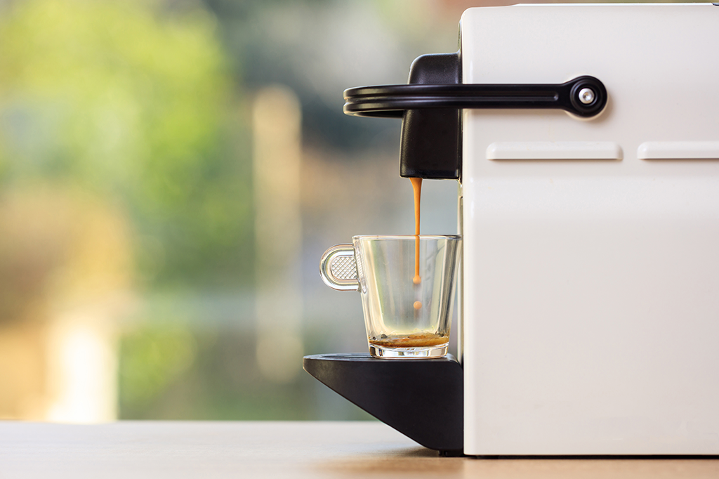 Foto mostrando uma máquina de café de capsula liberando café em uma xícara.