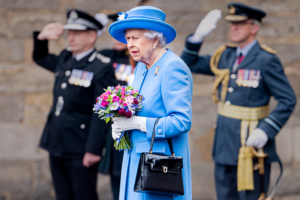 Foto da Rainha Elizabeth II carregando um buquê de flores e com sua bolsa pendurada no braço esquerdo.