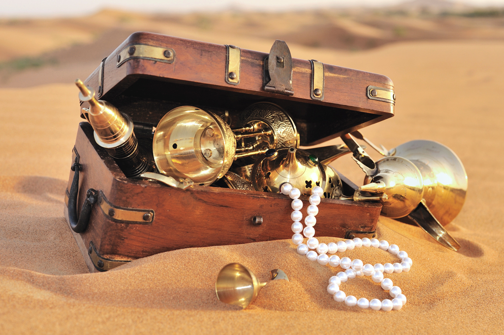 Foto de um baú cheio de tesouros em um deserto.