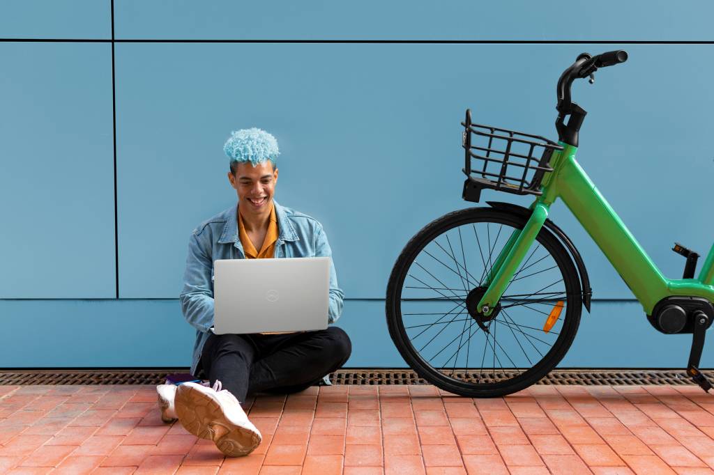 Homem sentado no chão ao lado de bicicleta verde enquanto usa Notebook Dell Inspiron 15 3000 Series.