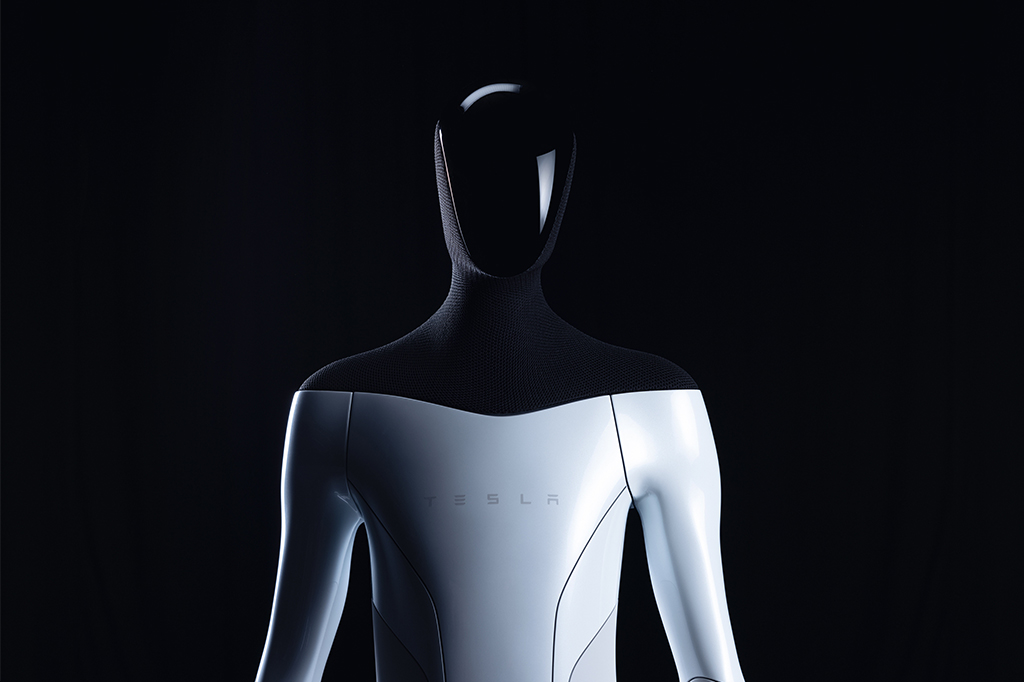 imagem do robô humanoide optimus, que possui a parte superior do seu corpo, até a altura dos ombros, preta, e a parte inferior é acinzentada, com Tesla escrito em seu peitoral