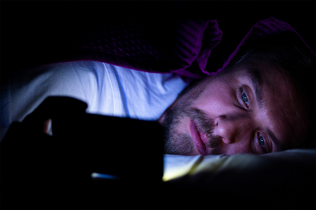 Homem deitado no escuro assistindo série no celular.