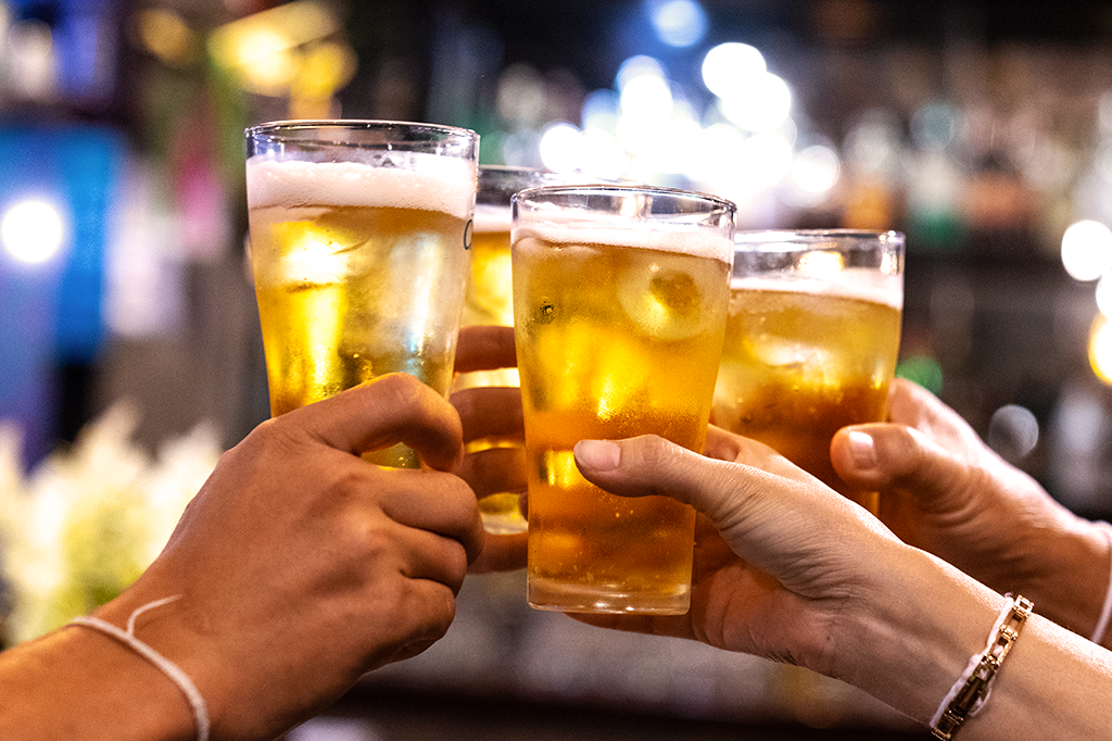 Foto de pessoas brindando com copos cheios de cerveja.