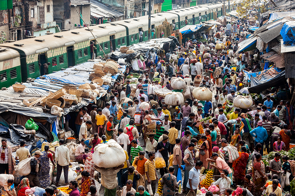 Mercado a céu aberto, cheio de pessoas, ao lado de trilhos de trem, na Índia.