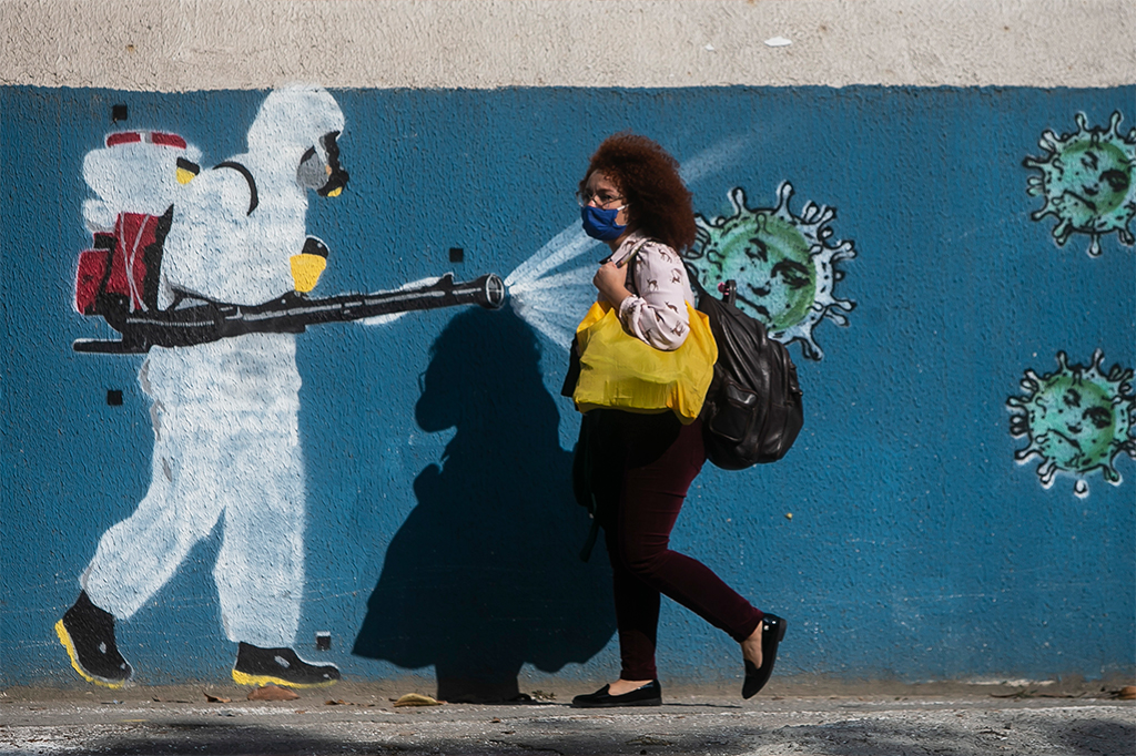 Mulher caminhando em frente a muro com grafite representando a sanitização da Covid-19.