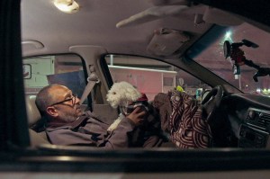 Foto de uma pessoa morando no carro com um cachorro, em cena do curta 