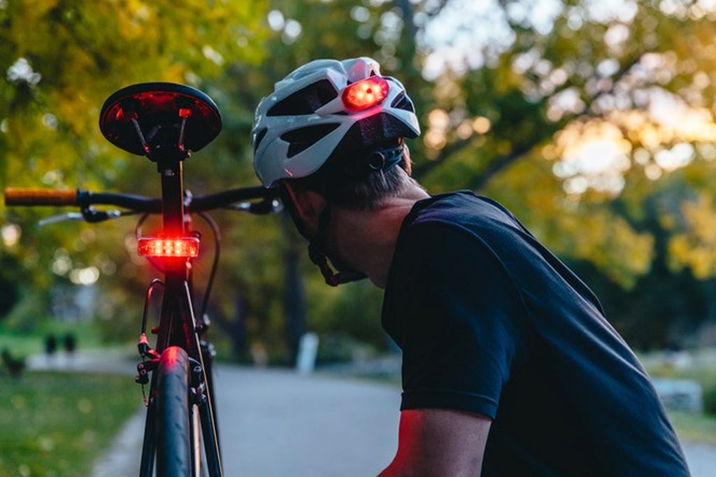 Foto de um homem utilizando capacete com luz, ao lado de sua bicicleta.