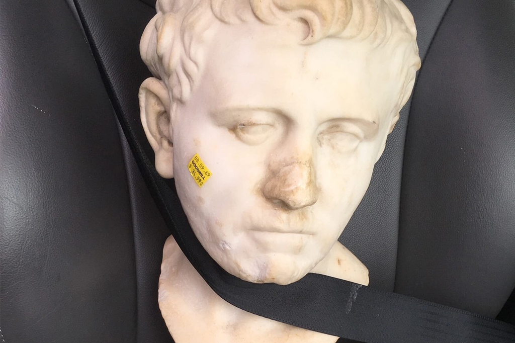 Escultura romana de busto presa em cinto de segurança de carro.