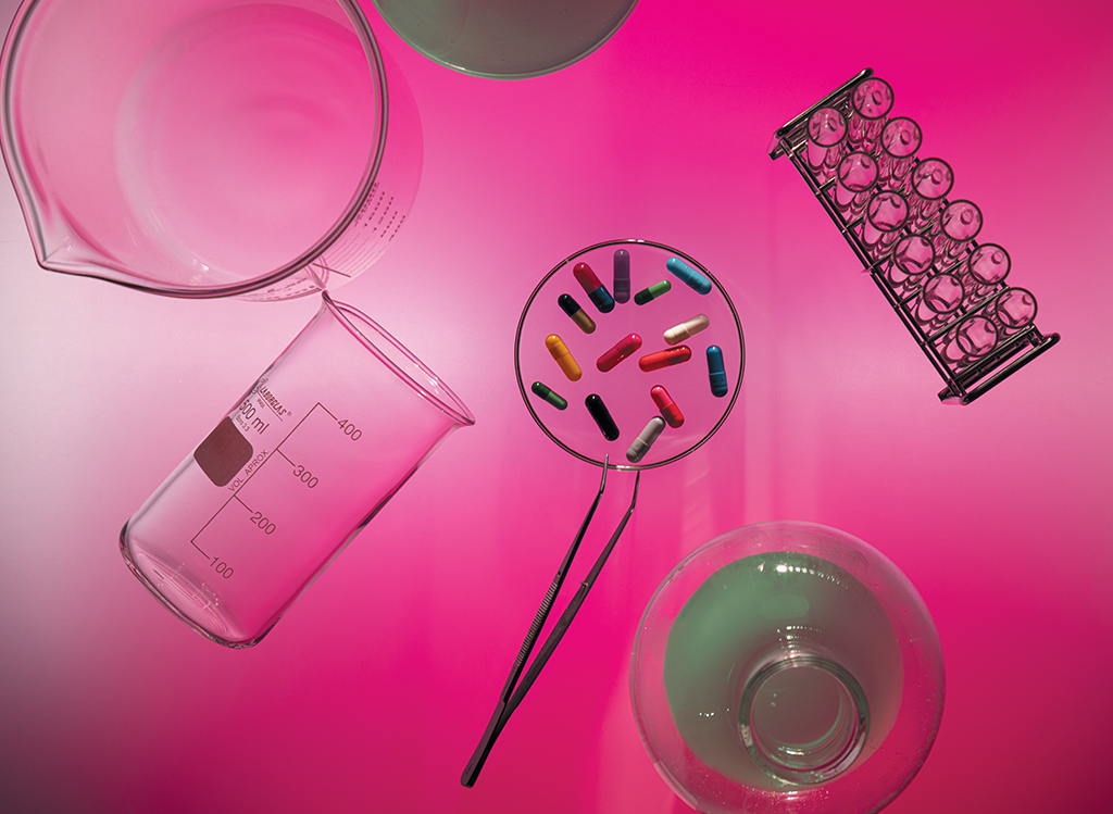 Foto de vidrarias de laboratório, com comprimidos de remédio no centro da imagem.