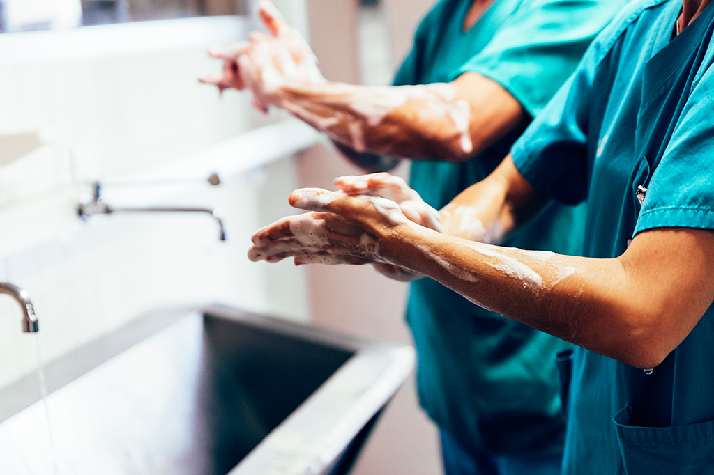 Duas pessoas médicas, uniformizadas, lavando as mãos.